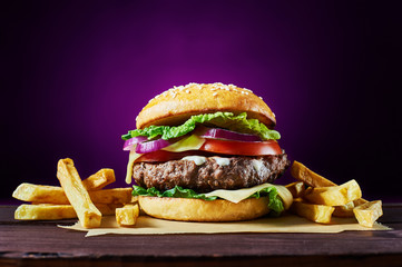 Craft beef burger and french fries on wooden table isolated on violet background.