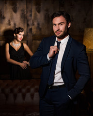 Handsome rich businessman with much money ready to marry elegant lady on background. Beautiful lady dreaming about luxurious life.