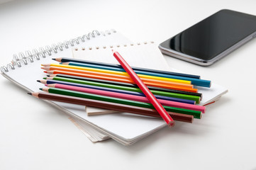 Fototapeta premium Notepad, color pencils and a phone on a light background
