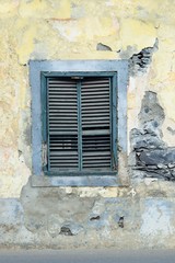 Fototapeta na wymiar Altes Holzfenster mit geschlossenen Schlagläden in einem verfallenen, sanierungsbedürftigen Haus