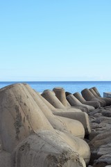Obraz na płótnie Canvas Mächtige Tetrapoden am Ufer zur Befestigung und zum Schutz der Küste, im Hintergrund das Meer, vor tiefblauem Himmel