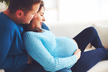 happy pregnant couple relaxing on couch at home