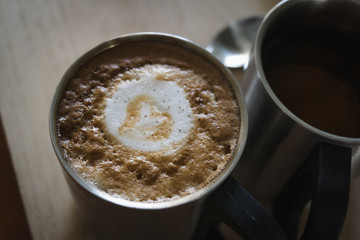 Hot dark coffee in stainless cup with cup of hot tea and stainless spoon on the wood. Dark coffee concept.