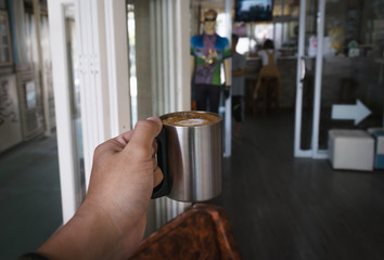Fototapeta na wymiar Hand holding hot dark coffee in stainless cup in asian coffee shop. Dark coffee concept.