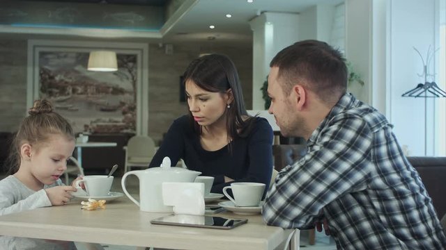 Family Enjoying tea In Cafe Together. Father and mother talking looking at their daughter.