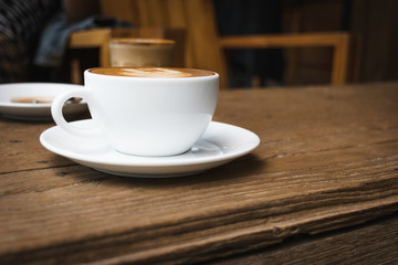 White cup of coffee on wooden table in the coffee shop.