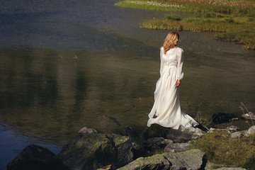 Sad bride posing in a mountain lake