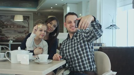 Beautiful young family taking selfie on smartfone while enjoying their time in cafe. - Powered by Adobe