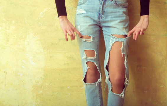 Feet trendy girl in torn jeans. Hands in pockets. Teenager and fashion. Clothes for young people. Clothing for teenagers. Slender girl in stylish denim pants with holes