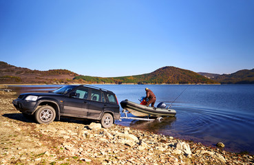 Fototapeta na wymiar Lake Tsonevo, Bulgaria - Circa October 2016: Mountain landscape. Mountain lake. All-road car pulls a motor boat on the water fishing