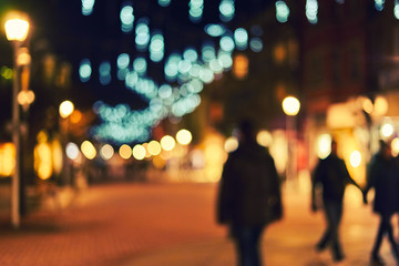 Blurred city street with their Christmas decorations. Trees decorated with bright garlands. People walking holidays. Bokeh basic background for design