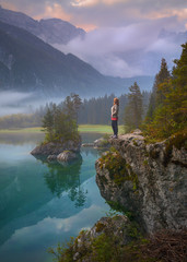 Female hiker standing next to the mountain lake at dawn