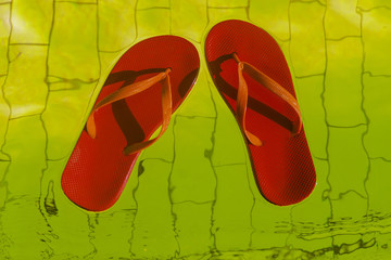 red flip-flops floating in a pool of yellow water, top view