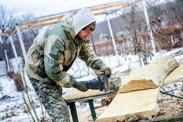 Beautiful strongman sawing a huge tree of chainsaw outdoors in winter