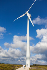 Fototapeta premium A young couple from near wind generators in field on a background beautiful clouds