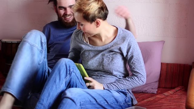 Loving couple sitting on the sofa and looking at tablet computer and laughing