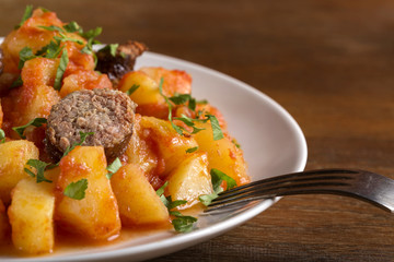 Potatoes stew with pork sausage and herbs on plate