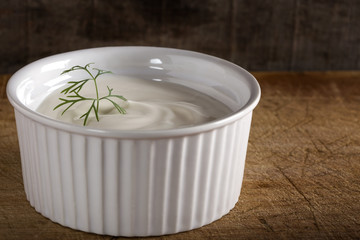 White bowl filled with sour cream on wood