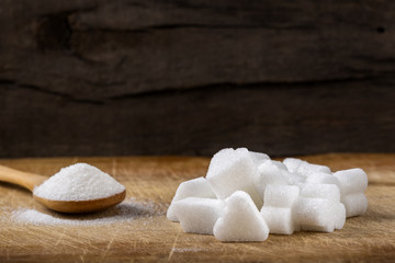 Heap of different sugar cubes shapes and wooden spoon filled with sugar