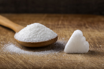 One sugar cube in heart shape and wooden spoon filled with sugar