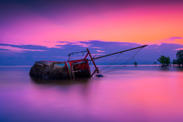 An old shipwreck or abandoned shipwreck, Boat capsized on beach in beautiful sunset background,...