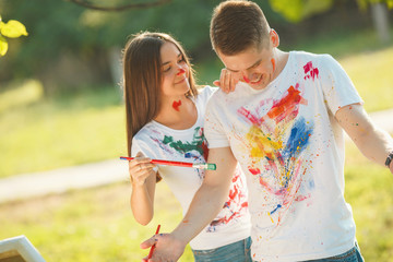 Pretty couple having fun at open air outdoors. Young man and woman drawing by colorful paints on...