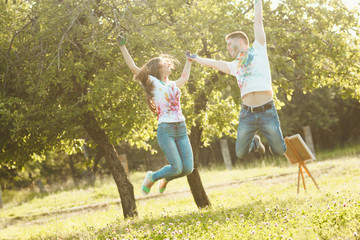 Smiling pretty couple jumping taking each other by the hand. Beautiful woman and handsome man having fun outdoors.