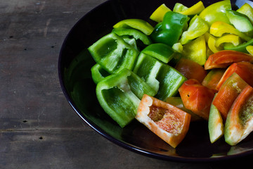 Red, yellow and bell peppers sliced in black plate on wood table