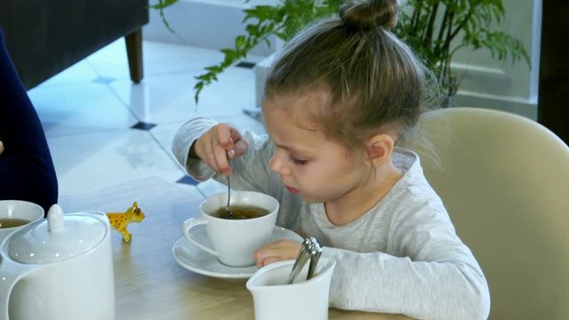 Little russian girl holding spoon and stiring sugar in tea at restaurant.