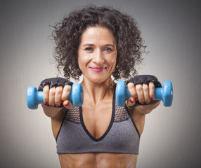 Beautiful fit woman lifting weights on gray background