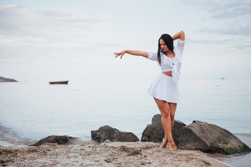 girl in frock dances barefoot on sand beach hands