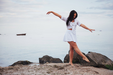 girl in frock dances barefoot on sand beach hands