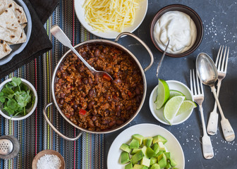 Beef and black bean chili bar on dark background, top view. Flat lay