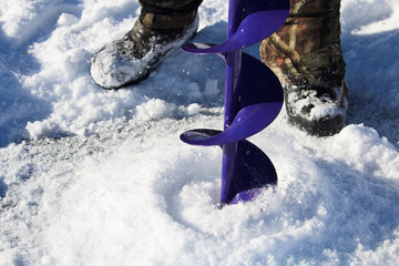 Drilling an Ice Fishing Hole With a Boots in the Background