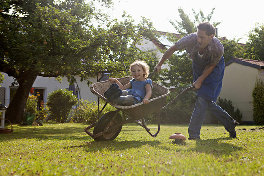 Father pushing wheelbarrow with daughter in the garden, Munich, Bavaria, Germany