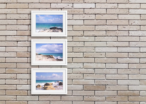 Frames with picturesque ocean view photos on decorative bricks wall. Interiors decor idea 