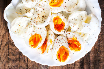 Hard boiled eggs, sliced in halves with black pepper spice on wooden background top view