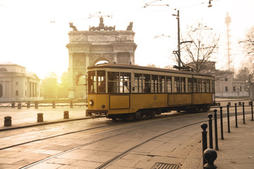 Old yellow tram passes, at dawn, in front of the Arch of Peace in Sempione Park, Milan, Italy.