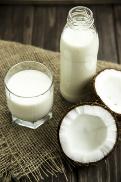 coconut milk in a glass next to the split in half coconut on sacking