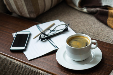 Cup of coffee Notepad glasses and a telephone. On the sofa lay a blanket and Slippers.