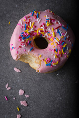 Pink frosted donut/doughnut with rainbow sprinkles. Gray background, top view. 