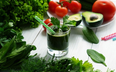 Green smoothies avocado cucumber and fresh herbs on a white wooden background.