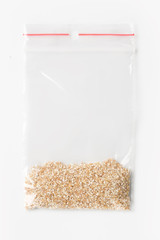 Plastic transparent zipper bag with a little raw wheat grits isolated on white, Vacuum package mockup with red clip. Concept