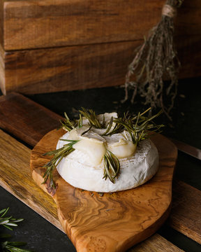 Close up vertical shot baked cheese camembert with rosemary on a wooden tray on a rustic dark background
