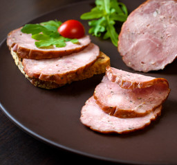 Smoked sausage, ham with red tomatoes and lamb's lettuce on a dark brown plate