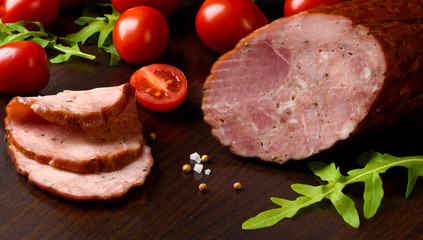 Smoked sausage, ham with red tomatoes and lamb's lettuce on a dark brown plate