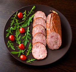 Smoked sausage, ham with red tomatoes and lamb's lettuce on a dark brown plate