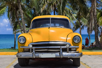 Gelber amerikanischer Oldtimer parkt unter Palmen am Strand in Varadero Kuba - Serie Kuba Reportage
