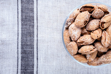 almond on glass plate on light grey linen napkin background, top view on right side