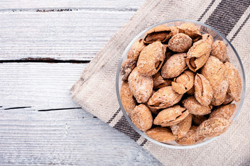 almond on glass plate on light grey linen napkin on white wooden background, top view on right side